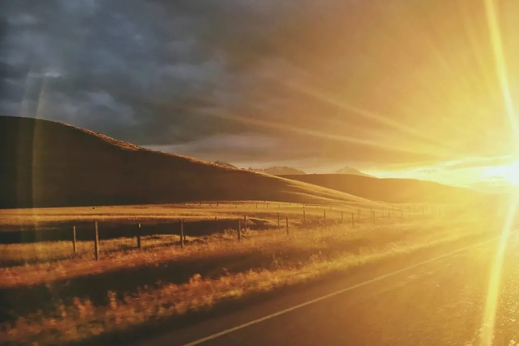 Yeni Zelanda'da uzanan çayırlar, tepeler ve gün batımına giden yol