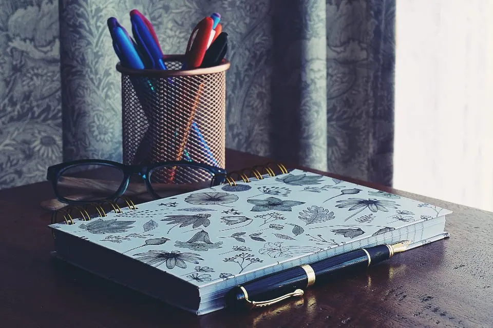 Çalışma masasında açık bir defter, kalemlik ve gözlük