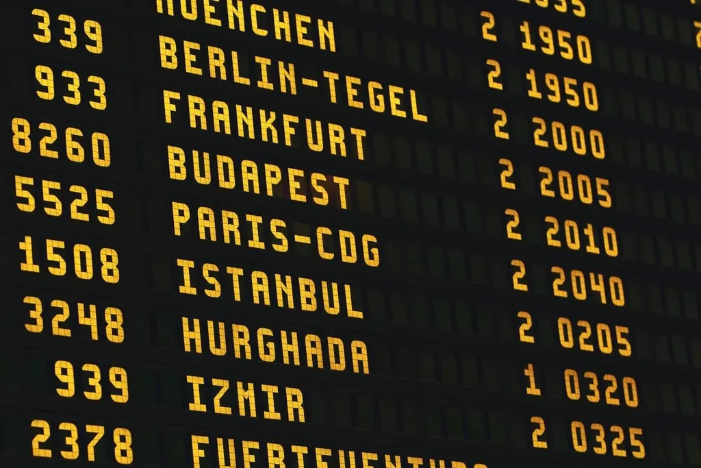 Painel eletrônico de partidas de aeroporto com números de voo, destinos e horários em letras amarelas sobre fundo escuro