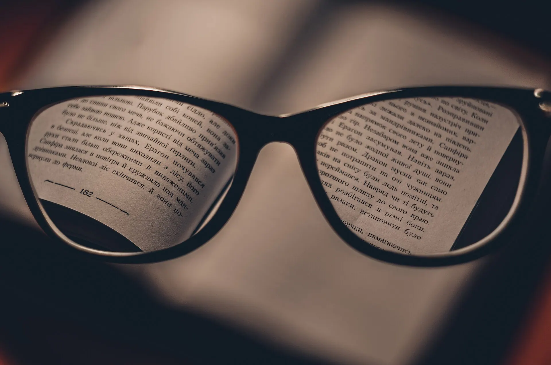Black-framed glasses held above an open book, the print sharp inside the lenses and blurred everywhere else