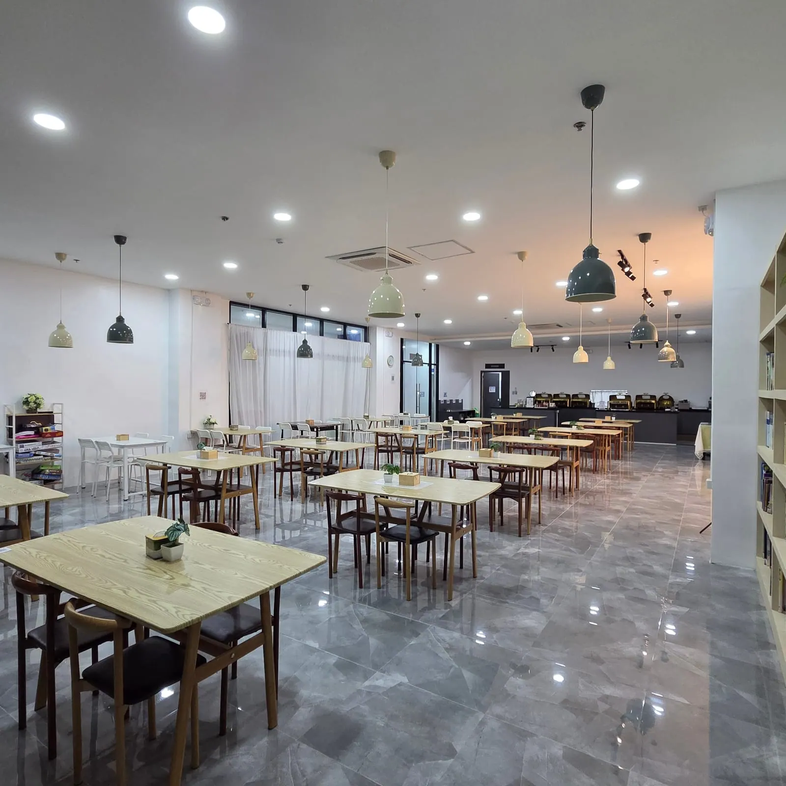 โรงอาหารของแคมปัสที่ยังไม่มีคน โต๊ะไม้และเก้าอี้เรียงเป็นแถว โคมไฟห้อยจากเพดาน มีเคาน์เตอร์บุฟเฟต์อยู่ด้านในสุดและชั้นหนังสือทางขวา
