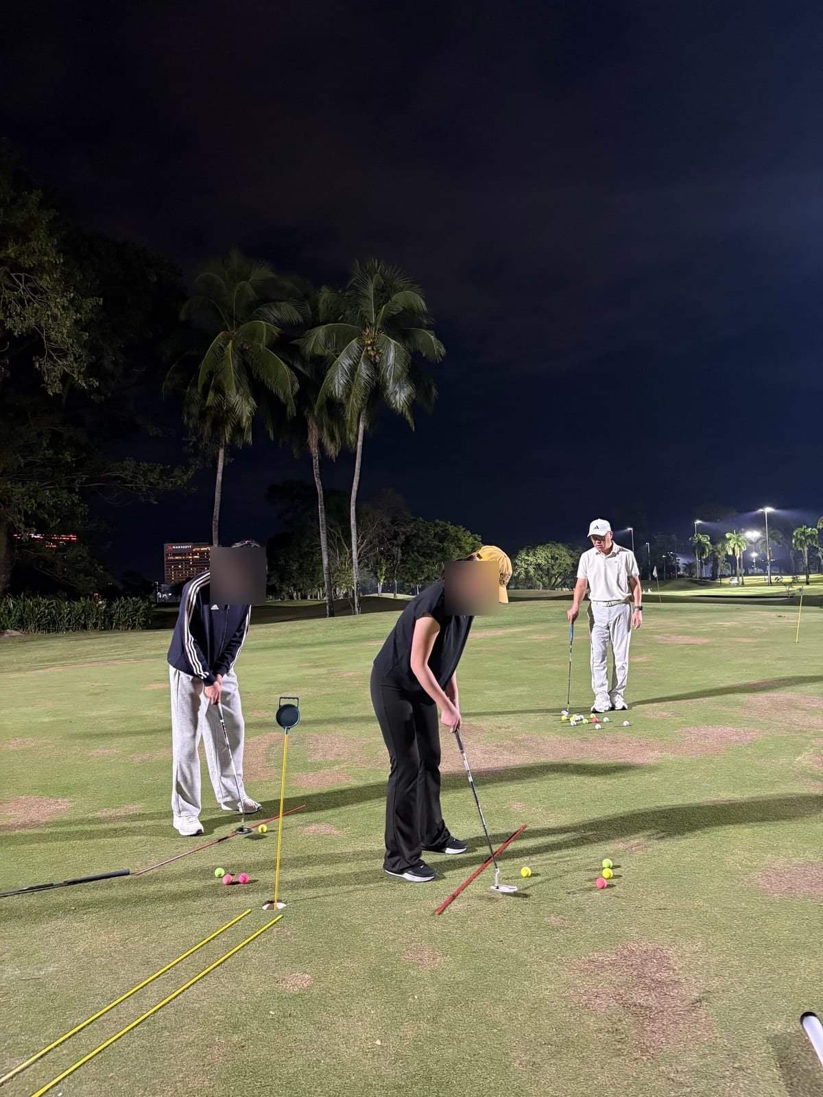 Two students practising putting while the pro watches
