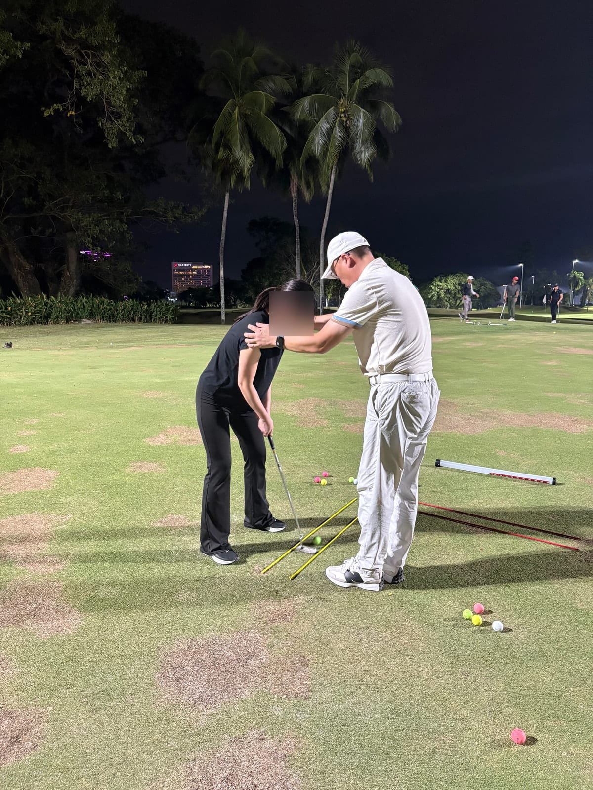 Teaching pro correcting a student’s putting posture on the green at night